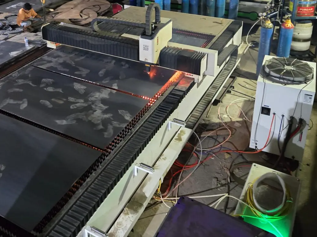 Mesin laser fiber CNC memotong plat besi di malam hari, dengan chiller dan tabung gas di sampingnya